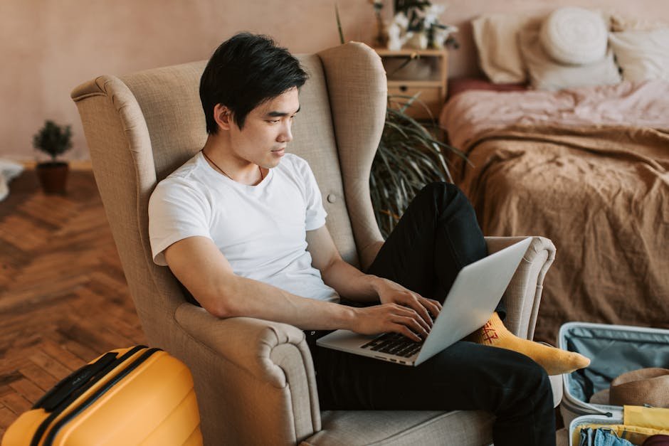 A man sitting comfortably in an armchair, using a laptop in a cozy home interior.