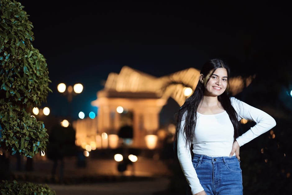 A young woman poses confidently outdoors at night with a lit building in the background.
