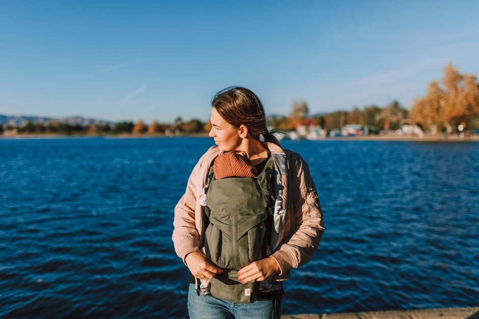 A mother with her baby in a carrier enjoys a sunny day by the water.