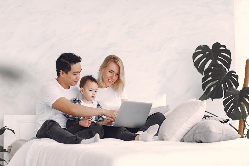 A joyful family with a child enjoying time together on a bed, using a laptop indoors.