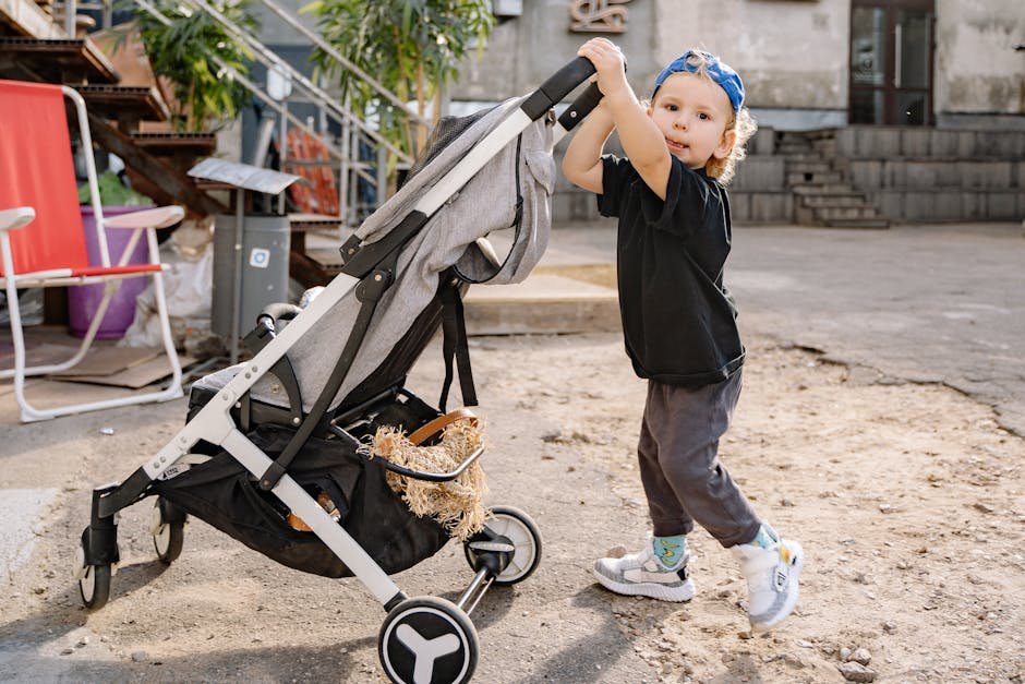 A playful child pushing a stroller in an urban yard setting on a sunny day.
