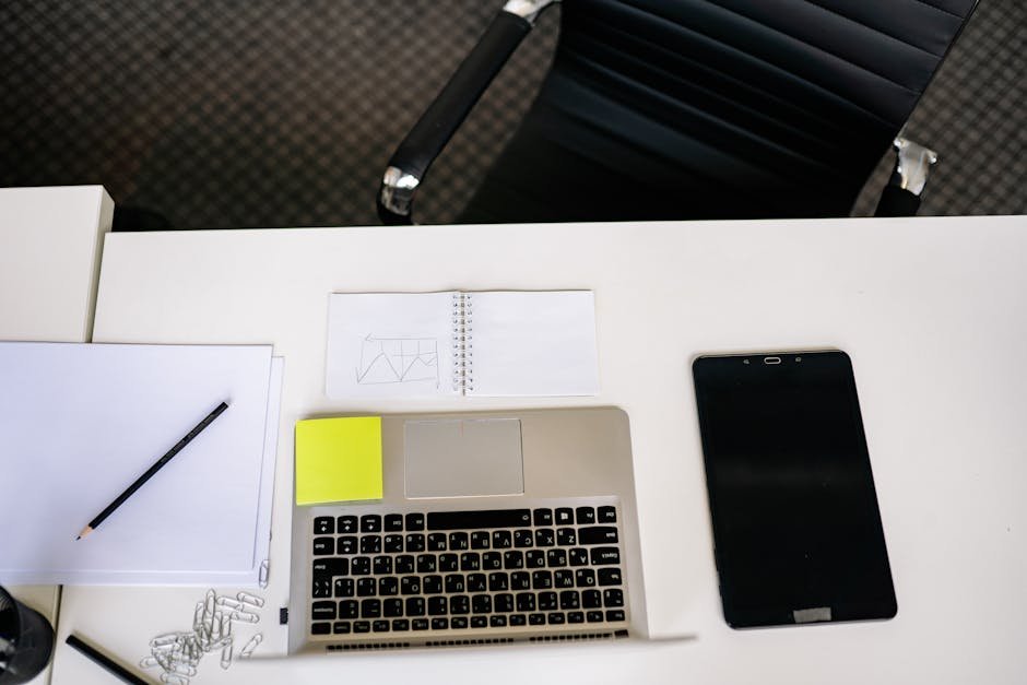Top view of a tidy office desk with laptop, tablet, and stationery.