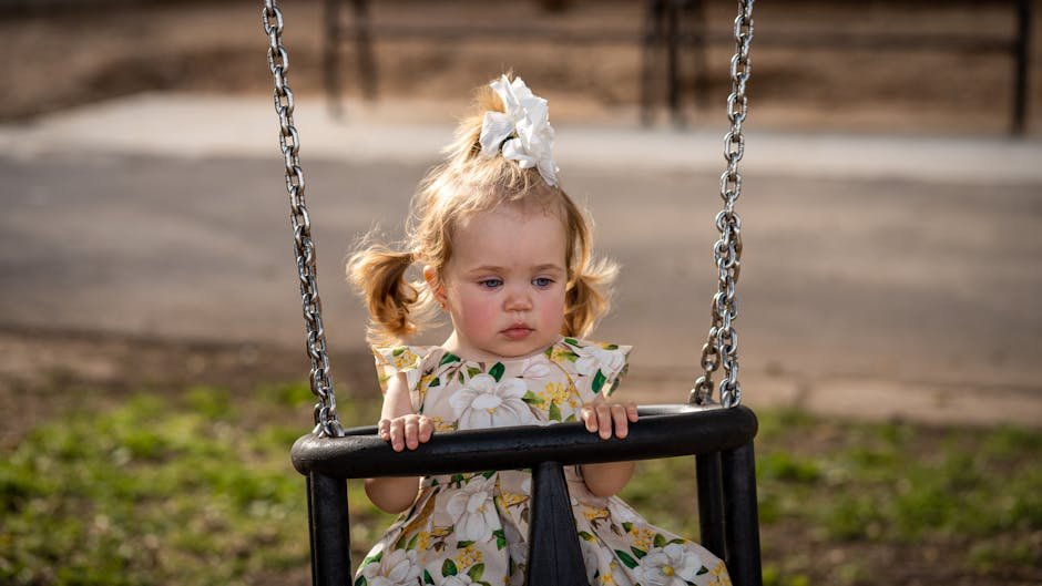 A cute toddler girl with pigtails and a floral dress on a swing in a sunny Los Angeles park.