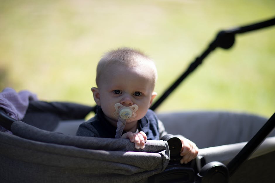 Adorable baby sitting in stroller outdoors with a pacifier, enjoying a sunny day in the park.