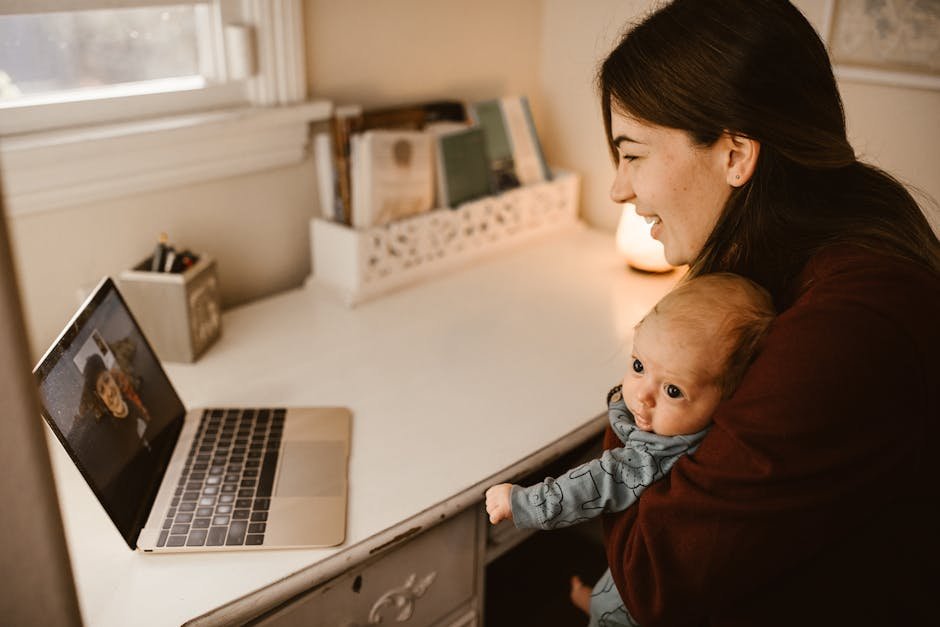 A mother using a laptop to video call a family member while holding her baby in a cozy home setting.