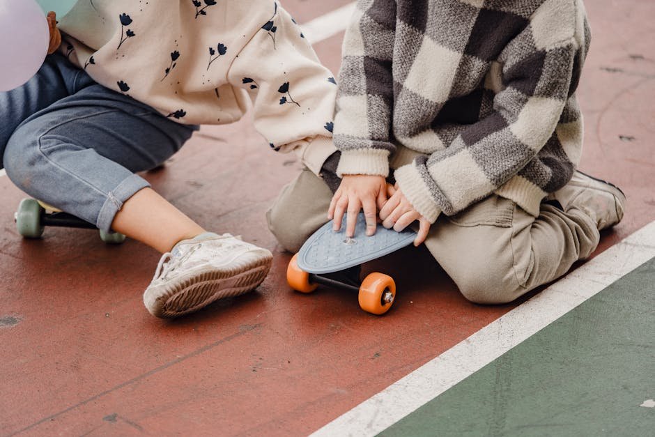 Crop faceless children in casual clothes sitting on skateboards on asphalt road in daytime