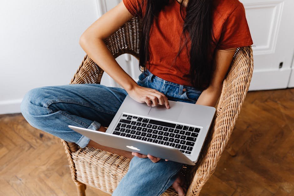 Young woman sitting on wicker chair using a laptop indoors, focusing on work.