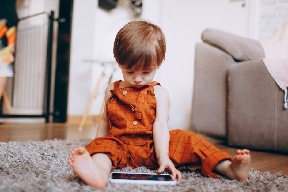 Adorable toddler in orange overalls interacting with a tablet on a cozy rug at home.