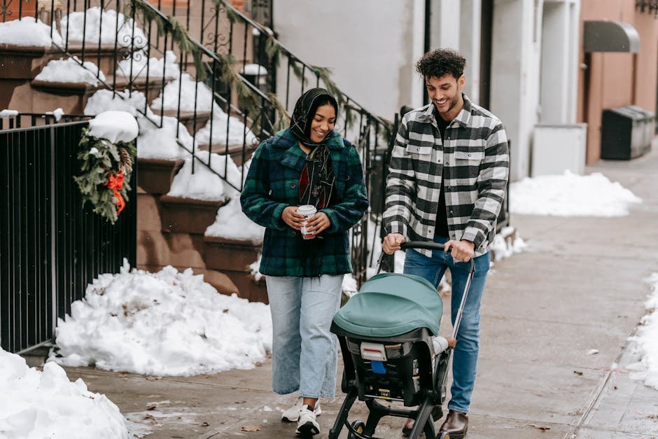 Full body of ethnic couple wearing casual clothes walking along sidewalk with stroller on street with Christmas decorations