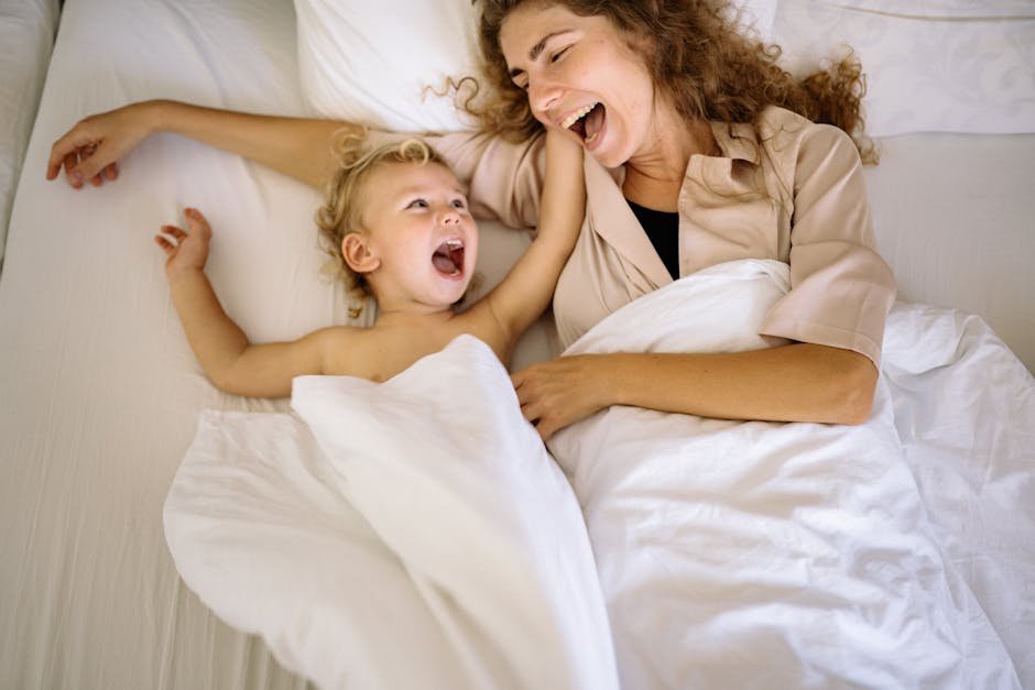 A joyful mother and child laughing together in a cozy indoor setting, wrapped in white blankets.